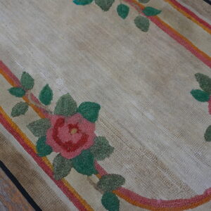 Beige floral rug detail showing pink roses, green leaves, and striped oval border on distressed wood flooring.