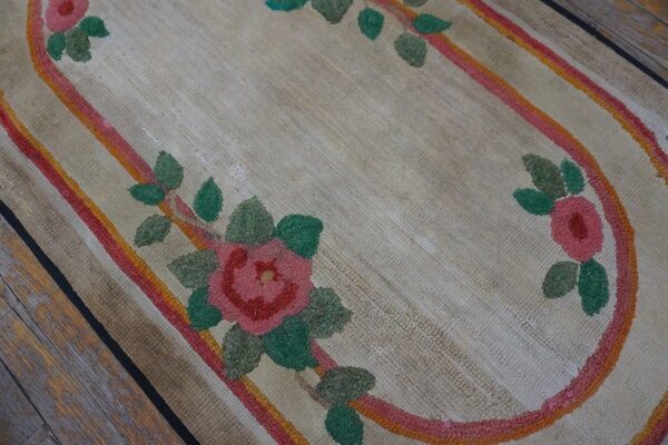 Beige floral rug detail showing pink roses, green leaves, and striped oval border on distressed wood flooring.