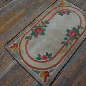 Low-pile beige rug with a central pink and orange floral oval on distressed wood planks.