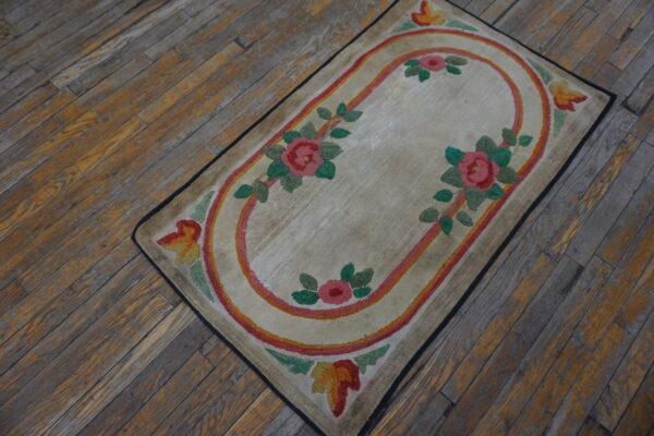 Low-pile beige rug with a central pink and orange floral oval on distressed wood planks.