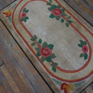 Low pile beige rug with pink, green, and orange floral border on distressed wood floor.