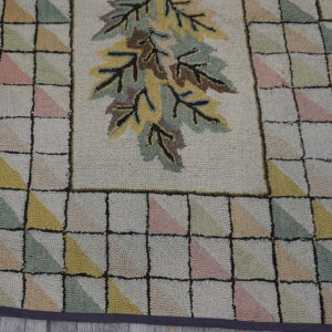 Textured rug with a central leaf design and geometric border of pale pink, green, and yellow triangles.