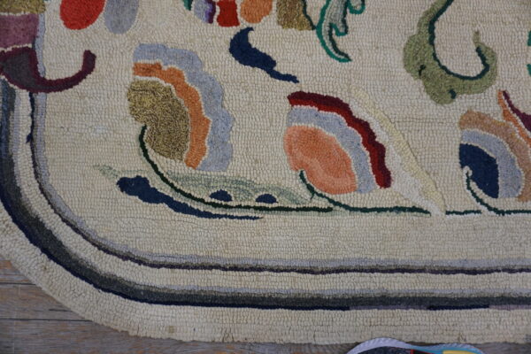 Cream hooked rug with multi-colored floral patterns rests on distressed wood flooring.