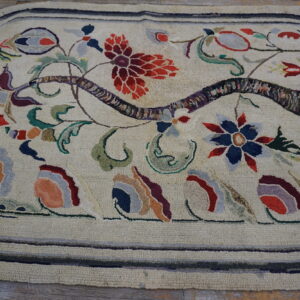 Rounded hooked rug featuring a multicolor botanical pattern on a cream field, visible on wood plank flooring.