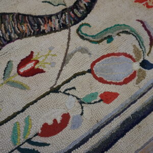Hooked rug close-up showing cream loops, red and gray florals, and a dark variegated striped pattern on wood floor.