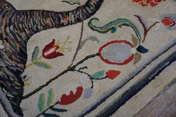 Hooked rug close-up showing cream loops, red and gray florals, and a dark variegated striped pattern on wood floor.