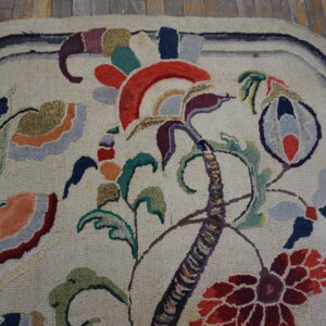 Cream hooked rug with a large stylized multi-colored floral pattern on worn wooden flooring.