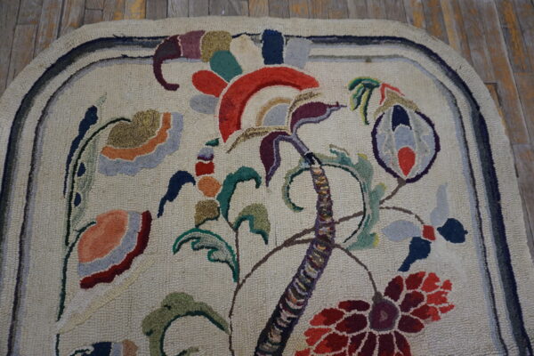 Cream hooked rug with a large stylized multi-colored floral pattern on worn wooden flooring.