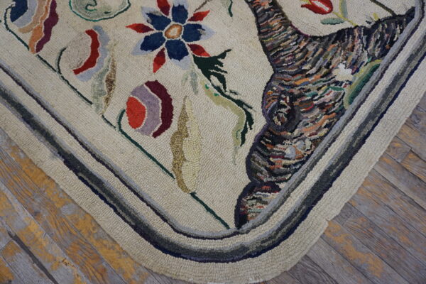 Textured beige rug corner displays colorful floral and abstract patterns with a striped border on distressed wood.