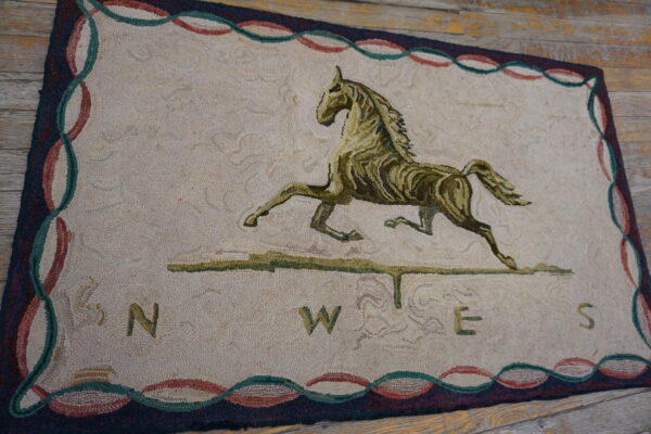 Beige rug featuring an olive green horse and compass design, bordered in red and teal, set on wood planks.