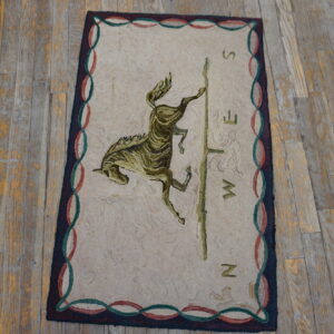 Beige hooked rug with an olive green horse motif and compass pattern on rustic plank flooring.