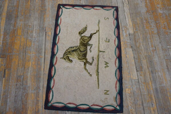 Beige hooked rug with an olive green horse motif and compass pattern on rustic plank flooring.