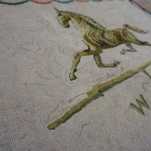 Detailed view of a dense cream rug with an olive-green running horse and compass pattern.