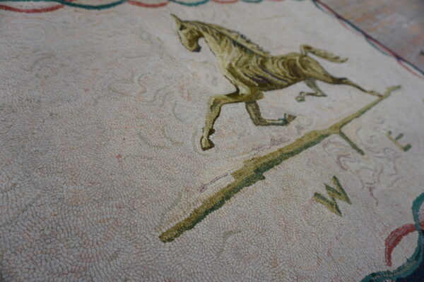 Detailed view of a dense cream rug with an olive-green running horse and compass pattern.