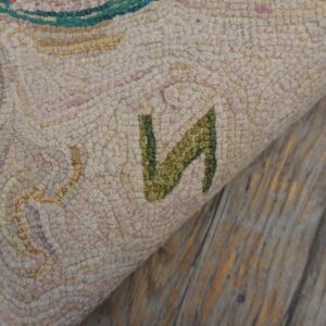 Highly textured light-colored rug with green and pink patterns folds over distressed gray wood flooring.