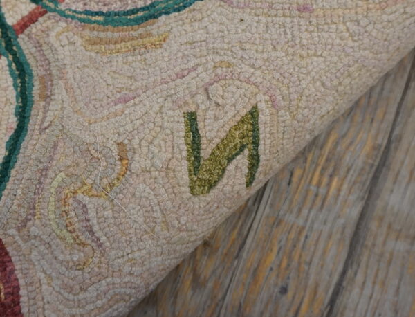 Highly textured light-colored rug with green and pink patterns folds over distressed gray wood flooring.