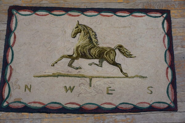 Cream and olive hooked rug featuring a running horse, compass points, and a multicolored serpentine border on wooden flooring.