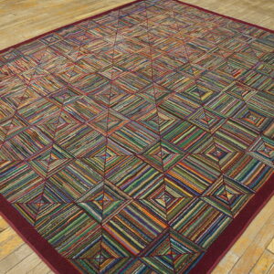 A large, colorful striped geometric rug with a solid burgundy border rests on light, distressed wood planks.