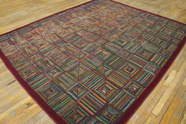 A large, colorful striped geometric rug with a solid burgundy border rests on light, distressed wood planks.
