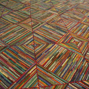 Close-up of a highly textured rug featuring diagonal multicolored strips forming large stitched geometric squares.