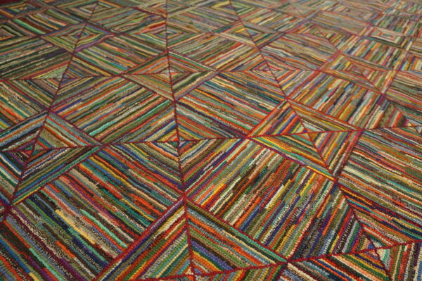 Close-up of a highly textured rug featuring diagonal multicolored strips forming large stitched geometric squares.