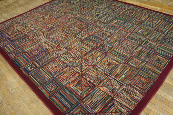 A vibrant geometric rug made of colorful woven strips, framed by a burgundy border on light wood planks.