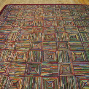 Highly textured multicolored rug with a geometric square pattern and burgundy border rests on wood planks.
