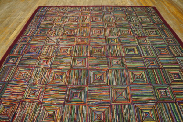 Highly textured multicolored rug with a geometric square pattern and burgundy border rests on wood planks.