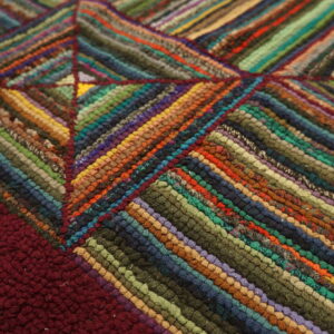 Multicolor braided rug detail showing diagonal stripes forming a geometric pattern next to a maroon section.