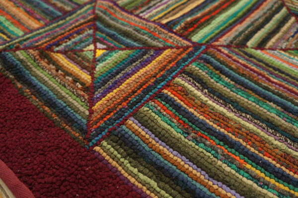 Multicolor braided rug detail showing diagonal stripes forming a geometric pattern next to a maroon section.