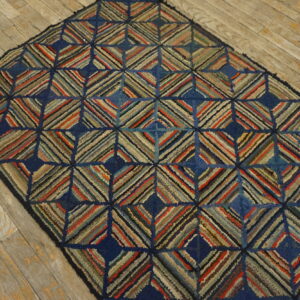 A dark blue hooked rug featuring multicolored striped diamonds rests on worn wooden floorboards.