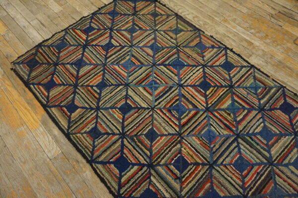A dark blue hooked rug featuring multicolored striped diamonds rests on worn wooden floorboards.