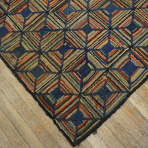 Textured blue and multicolored rug with a geometric diamond pattern rests on worn light wood flooring.