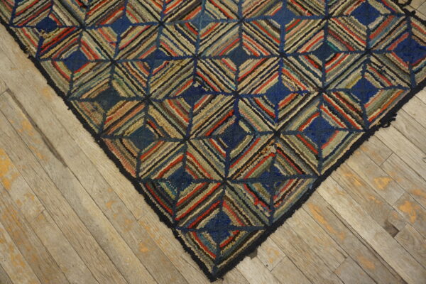 Textured blue and multicolored rug with a geometric diamond pattern rests on worn light wood flooring.