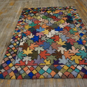 Multi-hued shaggy rug featuring large leaf shapes and a diamond border on distressed wooden floors.