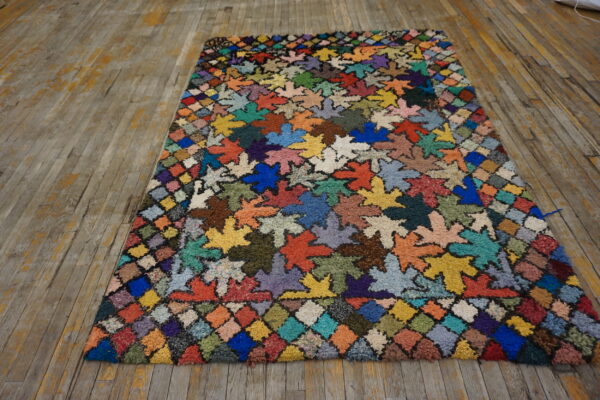 Multi-hued shaggy rug featuring large leaf shapes and a diamond border on distressed wooden floors.
