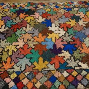 High-pile multicolored rug with a dense leaf pattern and patchwork border on wooden flooring.