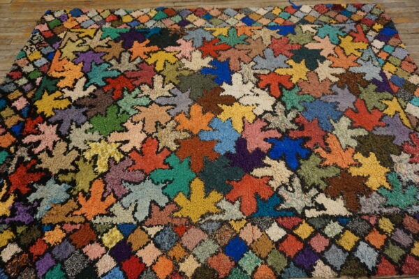 High-pile multicolored rug with a dense leaf pattern and patchwork border on wooden flooring.