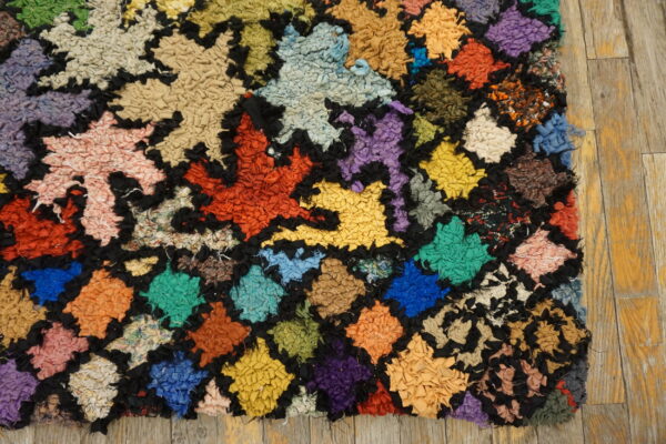 A multicolored, chunky-textured rag rug with a geometric grid pattern rests on worn wood flooring.