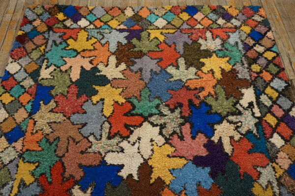 Colorful textured rug featuring large leaf shapes and a checkered border on rustic wooden floorboards.