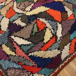 Multicolored rag rug with high pile and abstract swirling shapes rests on light wooden plank flooring.