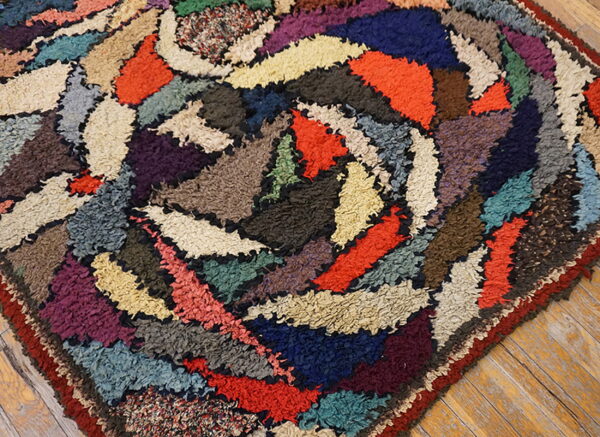 Multicolored rag rug with high pile and abstract swirling shapes rests on light wooden plank flooring.