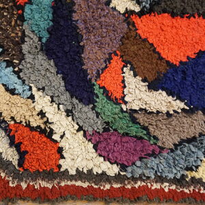 Shaggy multicolor rug featuring a radial pattern with textured patches of rust, navy, orange, green, and cream.
