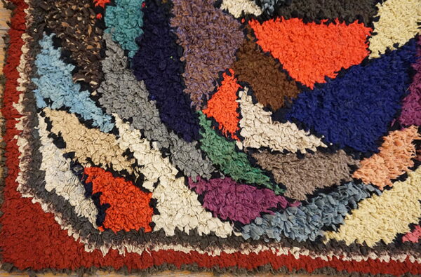 Shaggy multicolor rug featuring a radial pattern with textured patches of rust, navy, orange, green, and cream.