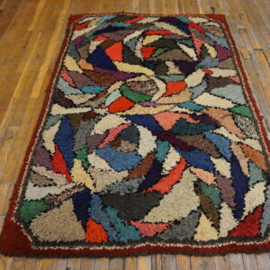 Multicolored patchwork rug with high shaggy pile and a red border rests on a rustic wood plank floor.