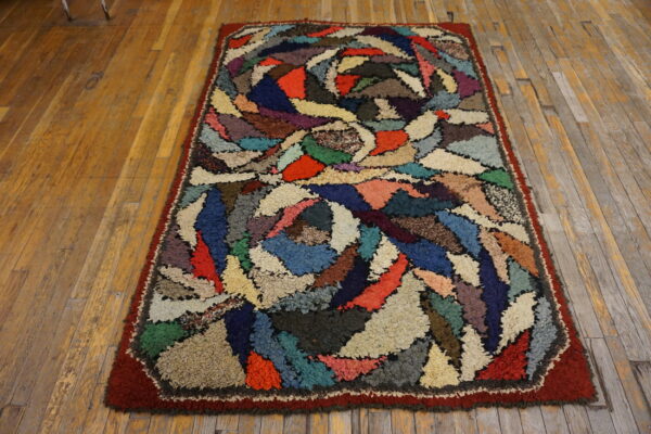 Multicolored patchwork rug with high shaggy pile and a red border rests on a rustic wood plank floor.