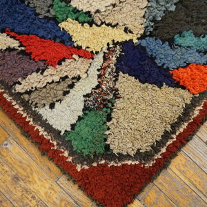 Shaggy multicolored rug corner in geometric blocks of blue, red, green, and cream on rustic wood floors.