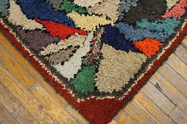 Shaggy multicolored rug corner in geometric blocks of blue, red, green, and cream on rustic wood floors.