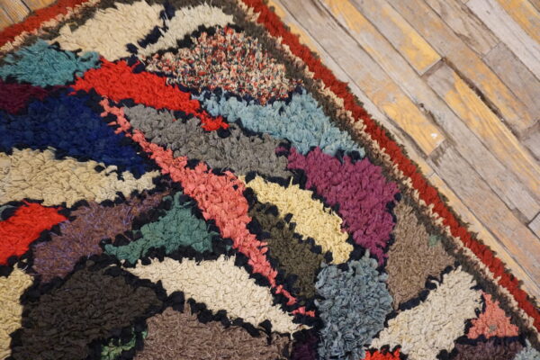 Detail of a highly textured, multicolored rug with irregular, dark-outlined shapes on distressed flooring.