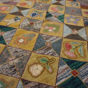 Patchwork rug featuring gold squares with colorful floral motifs interspersed with variegated triangular blocks.